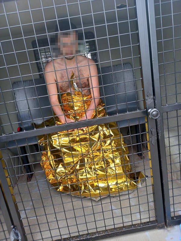 Ujęty mężczyzna okryty kocem termicznym w&nbsp;przedziale przewozowym radiowozu