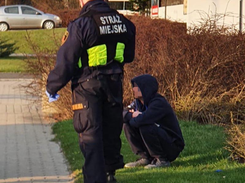 Strażnik miejski stojący przy kucającym na trawniku mężczyźnie