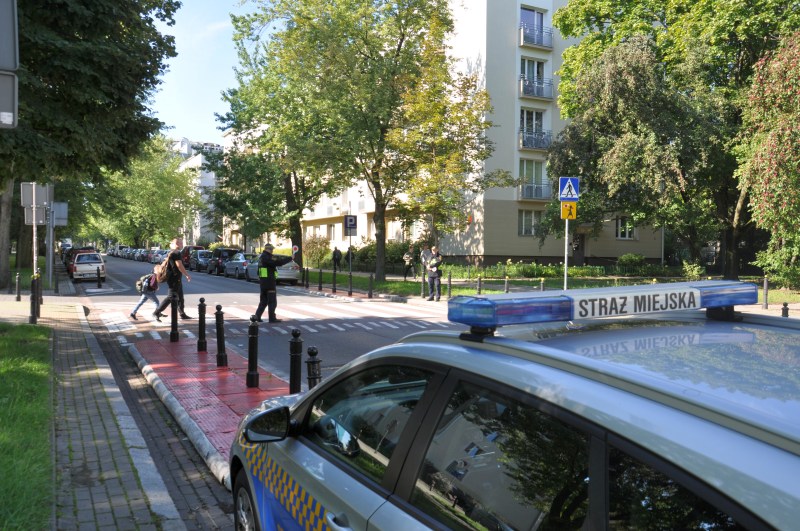 Strażnik miejski przeprowadzający przez jezdnię matkę z&nbsp;dzieckiem wracających ze szkoły