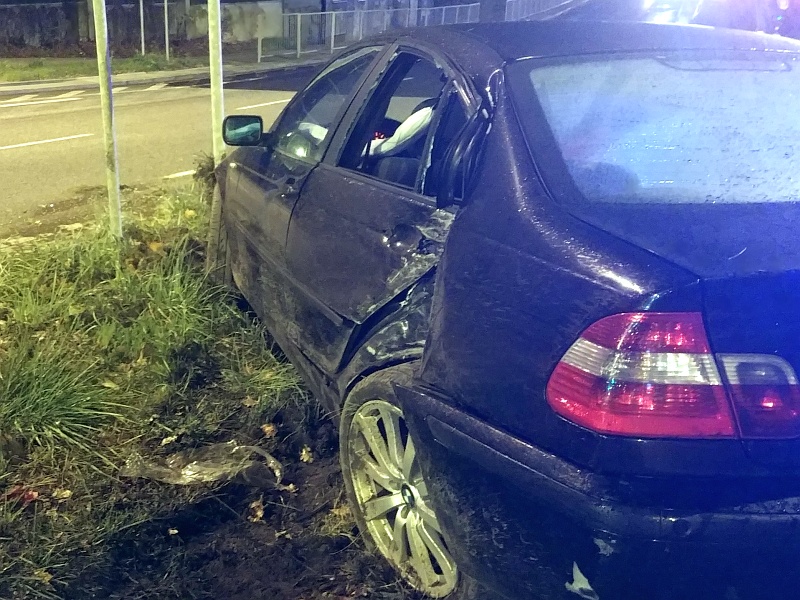 Zdjęcie z&nbsp;interwencji: widoczne od tyłu czarne BMW stojące na pasie zieleni. Ma rozbity lewy tylny bok, a&nbsp;przód wbity w&nbsp;słupek znaku drogowego.