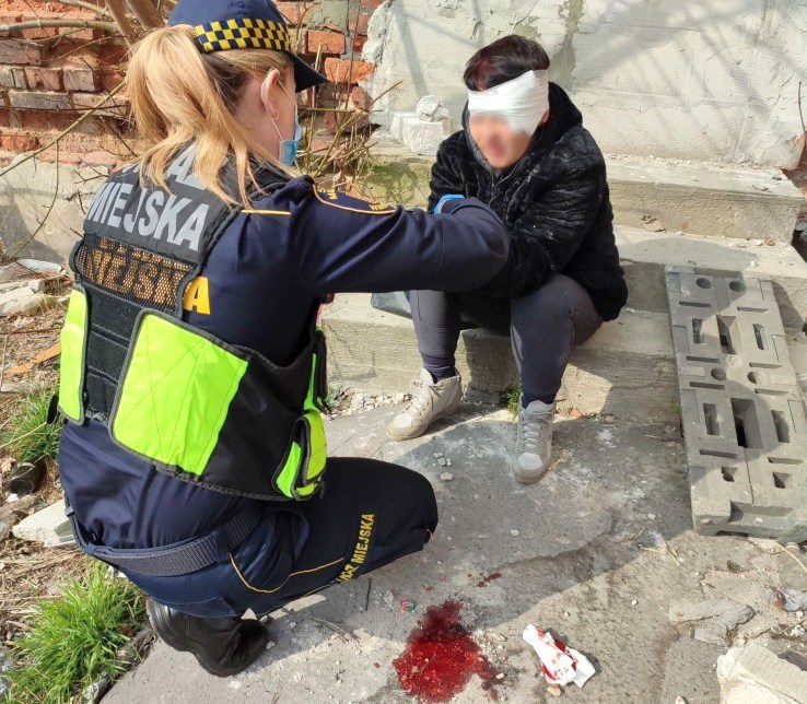 Zdjęcie z interwencji: strażniczka miejska opatruje siedzącą na ziemi kobietę, która ma już na głowie bandaż.