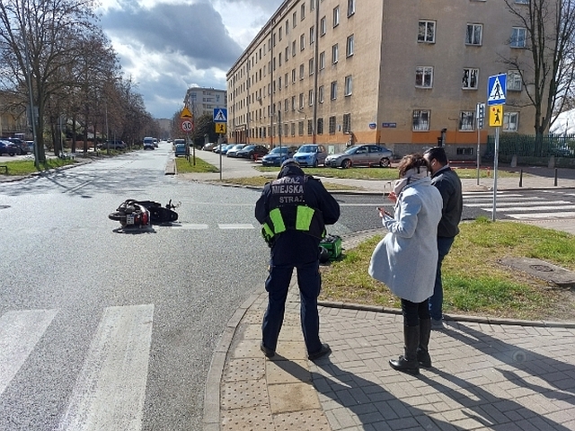 Zdjęcie z interwencji: na chodniku stoi strażnik miejski, obok niego kobieta i mężczyzna. Nieco dalej, na skrzyżowaniu, leży przewrócony skuter.