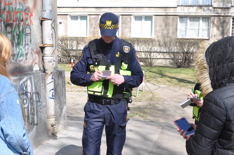 Strażnik miejski legitymujący grupkę nieletnich, stojących po jego prawej i lewej stronie