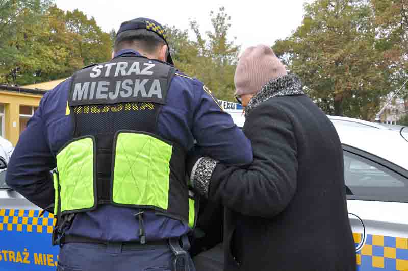 Strażnik miejski prowadzący pod rękę starszą kobietę