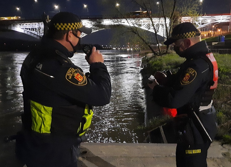 Zdjęcie ilustracyjne: patrol straży miejskiej na bulwarach wiślanych nocą. W tle jasno oświetlony most Śląsko-Dąbrowski.