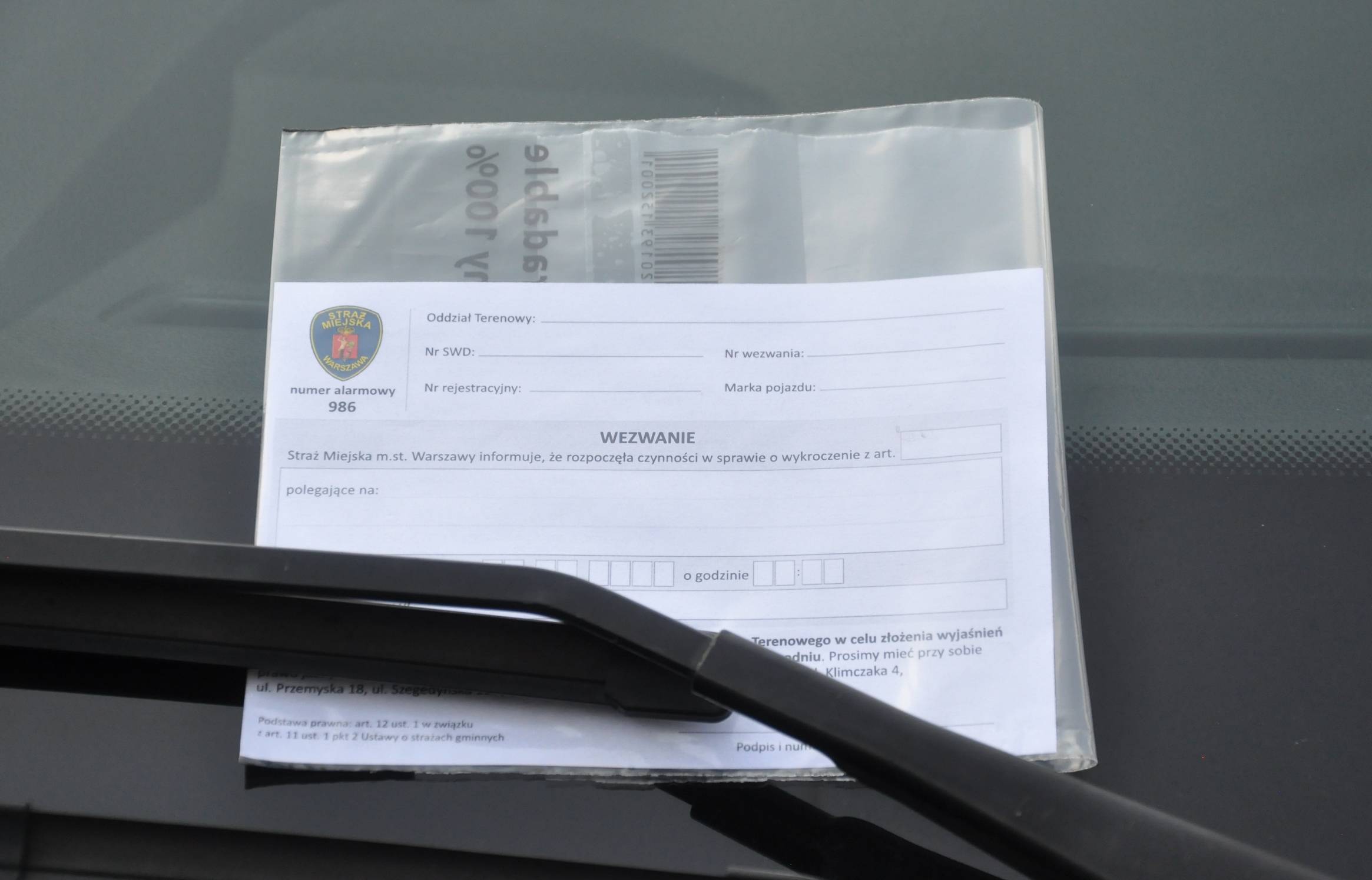 Wezwanie dla kierowcy za wycieraczką na szybie samochodu.