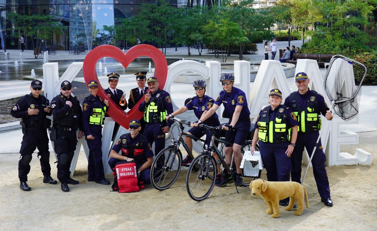 Zbiorowe zdjęcie strażników miejskich z&nbsp;różnych formacji warszawskiej Straży Miejskiej na tle napisu "Kocham Warszawę", pl. Europejski.