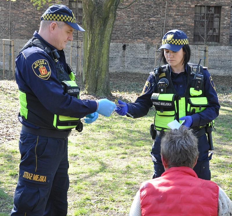 Patrol straży miejskiej legitymuje siedzącą kobietę.