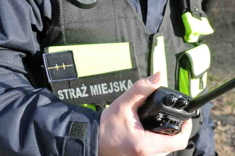 Detal: strażnik miejski trzymający w ręku radiotelefon.