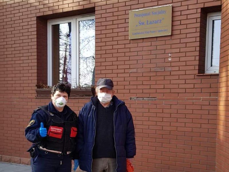 Bezdomny w&nbsp;towarzystwie strażniczki przed pensjonatem socjalnym