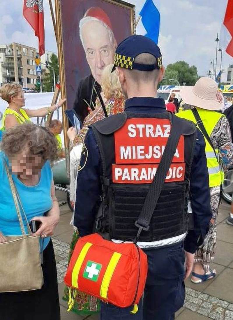 Uroczystości beatyfikacji kard. Wyszyńskiego- strażnik miejski z&nbsp;kamizelką "Paramedic" i&nbsp;apteczką przewieszoną przez ramię stojący przed portretem Prymasa.