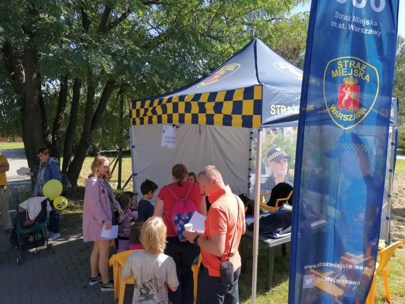Stanowisko straży miejskiej na pikniku. Pod daszkiem stolik z&nbsp;kolorowankami dla dzieci, przed namiotem grupka dzieci z&nbsp;rodzicami.