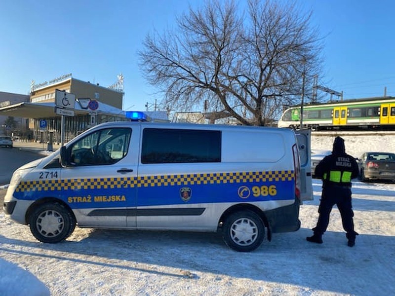 Zdjęcie z&nbsp;interwencji: strażnik miejski przy radiowozie stojącym w&nbsp;pobliżu Dworca Wschodniego. W&nbsp;tle, na nasypie, przejeżdża pociąg.