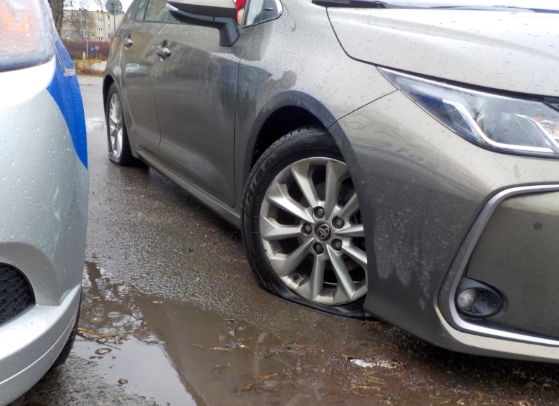 Zdjęcie z interwencji: uszkodzone prawe przednie koło grafitowej toyoty. Widoczna płaska opona.