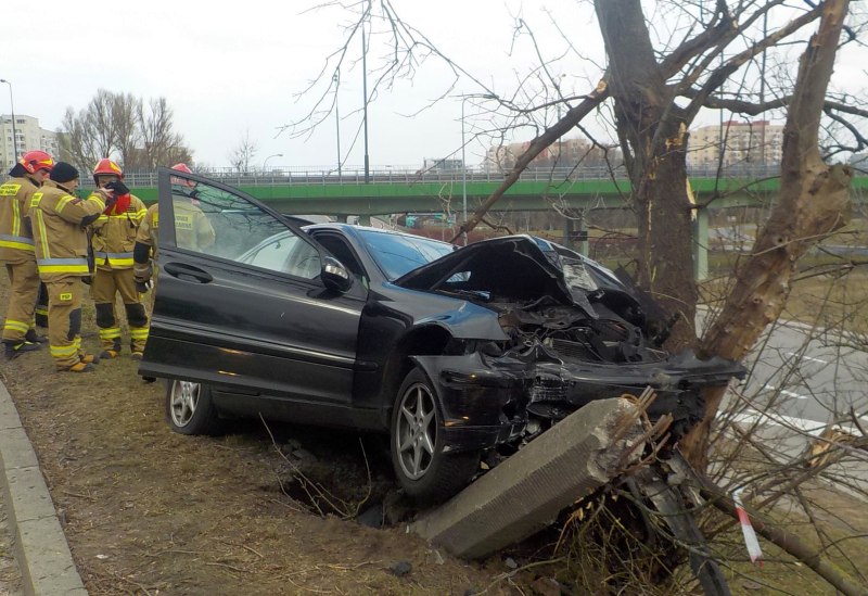 Zdjęcie z&nbsp;interwencji: czarny mercedes wbity przodem w&nbsp;drzewo. W&nbsp;tle grupka strażaków.