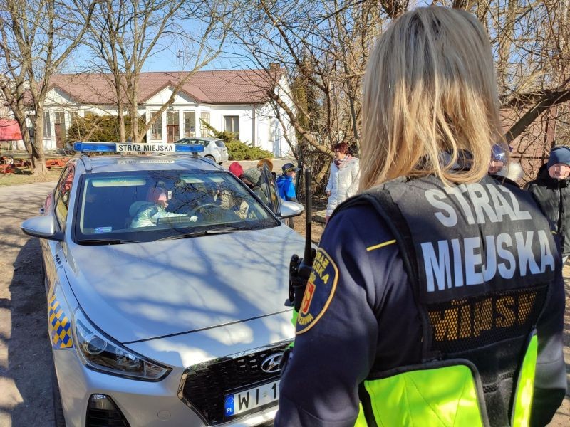 Zdjęcie ze spotkania ukraińskich dzieci ze strażnikami: na pierwszym planie strażniczka miejska, w tle radiowóz z siedzącymi w nim dziećmi.