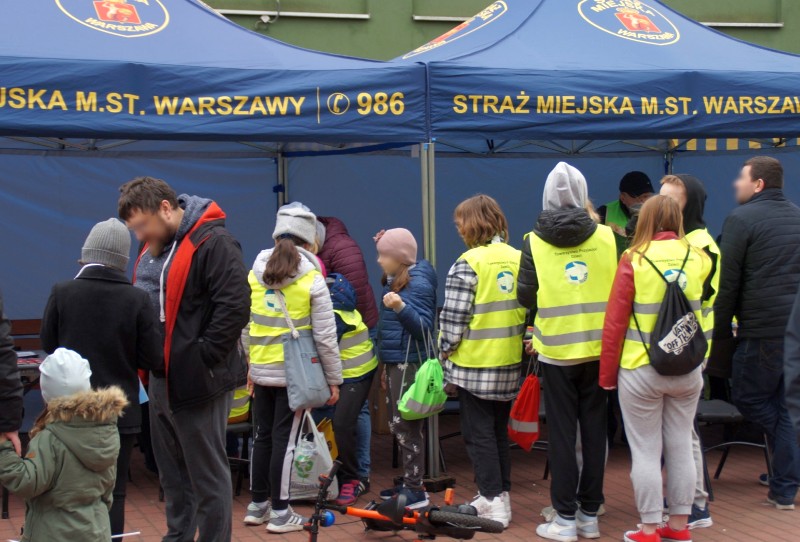 Grupka młodzieży przed stanowiskiem Straży Miejskiej na pikniku plenerowym.