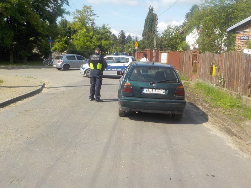 Samochód nietrzeźwego kierowcy stojący na jezdni. Obok niego stoi strażnik miejski, w tle- radiowóz straży miejskiej.