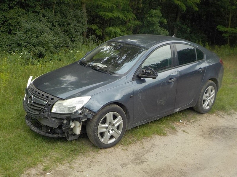 Szary opel porzucony na leśnej drodze.