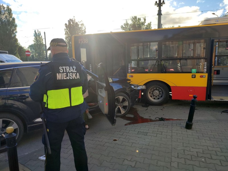 Strażnik miejski na miejscu kolizji. Za nim czarny samochód, który uderzył a autobus miejski.