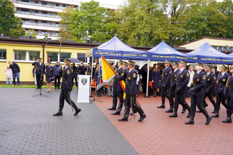 Poczet sztandarowy oraz kompania reprezentacyjna Straży Miejskiej m.st. Warszawy defiluje przez zaproszonymi gośćmi.