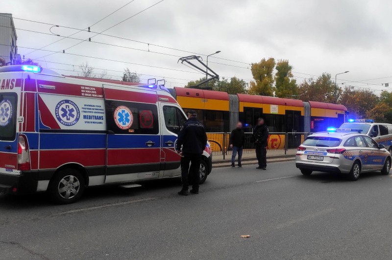 Karetka pogotowia stojąca przy przystanku tramwajowym. Obok niej strażnik miejski. W tle radiowozy straży miejskiej.