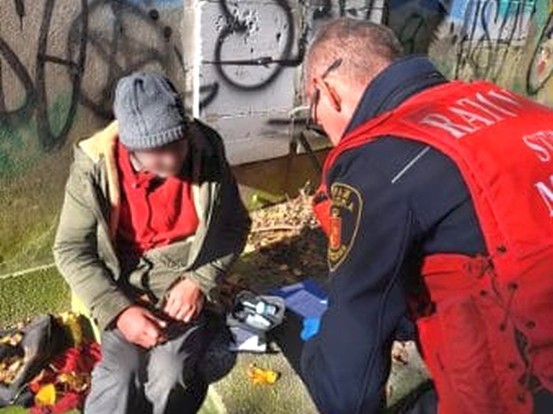 Strażnik miejski w kamizelce "ratownik medyczny" bada bezdomnego.